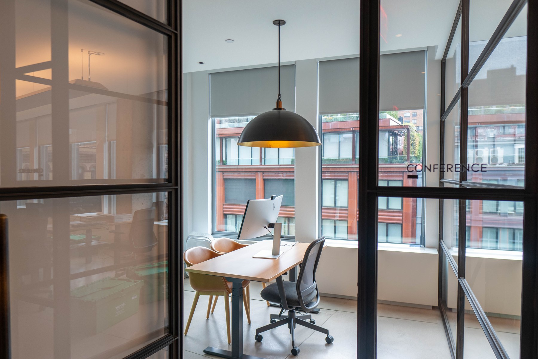 A conference room seen through black steel-framed glass, a pendant lamp over the table, Art Basel NY Headquarters