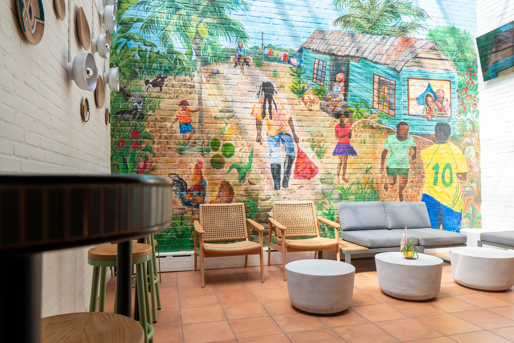 A painted mural covering the full brick back wall of the patio, with cane armchairs, an upholstered outdoor sofa and round concrete tables on terracotta tile