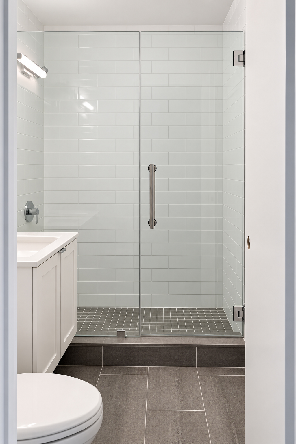 Walk-in shower behind a frameless glass door, white wall tile to the ceiling and a mosaic floor on a tiled curb