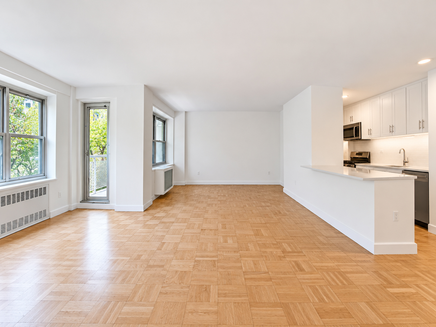 Open living room with parquet floor, windows and a balcony door on the left, and the kitchen counter on the right